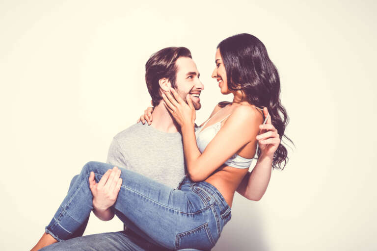 Happy man in t-shirt holding woman in jeans and bra touching his